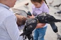 Close-up children feeding feral pigeons in the city park during family outing