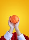 Close up children hands holding an orange fruit isolated over yellow background. Chinese New Year celebration concept Royalty Free Stock Photo