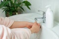 Close-up of children`s, women`s hands in a pink bathrobe under the turned on tap with water in the bathroom. Hand washing. Royalty Free Stock Photo