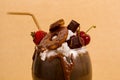 Close up of chocolate indulgent extreme milkshake with brownie cake, strawberries, cherries, and a plastic straw with