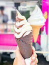 Close-up chocolate and vanilla twist soft serve in a dark chocolate crispy waffle cone in human hand with blurry background. Royalty Free Stock Photo