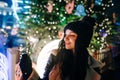 Close-up Christmas portrait of a lady in warm clothes lights a sparkler on the background of a street Christmas tree, looks away Royalty Free Stock Photo