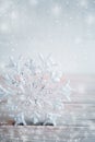 Close-up Christmas toy snowflake is standing on wooden table on light grey background with snow. Royalty Free Stock Photo