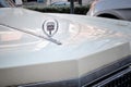 Close-up of a chrome-plated nameplate on the hood cover of a retro Cadillac car of beige color in a parking lot in the city