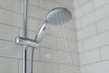 Close-up of chrome shower, faucet, in the bathroom covered decorative ceramic tiles with white glossy bricks. Water running from s Royalty Free Stock Photo