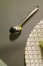 Close up of a chrome spoon with a silver plate on one side on a transparent glass table