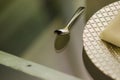 Close up of a chrome spoon with a silver plate on one side on a transparent glass table