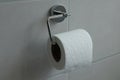 Close up of a chrome toilet roll holder with a white toilet roll in a grey tiled bathroom Royalty Free Stock Photo