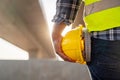 Close up of Civil engineer's hand holding yellow safety helmet at road construction site. Safety First concept