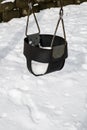 Close up of classic swing in a public park on a snowy day, black rubber baby swing seat on a metal chain