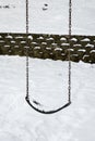 Close up of classic swing in a public park on a snowy day, black rubber swing seat on a metal chain