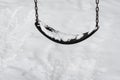 Close up of classic swing in a public park on a snowy day, black rubber swing seat on a metal chain