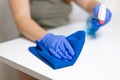 Young woman housekeeper is cleaning, wiping down table surface with blue gloves, wet rag, spraying bottle cleaner. COVID Royalty Free Stock Photo