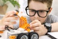 Close-up of a clever boy in eyeglasses builds and programs a robot car at home. The child is learning coding and