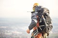 Close-up of a climber from the back in gear and with a backpack with equipment on the belt, stands on a rock, at high