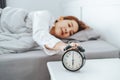 Close up Clock on the bed Asian woman wake up and disturbed by alarm clock early morning Royalty Free Stock Photo