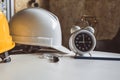 Close up of clock and engineering safety helmet on blueprint table. Architecture and engineering equipment concept. Construction