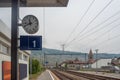 Close up of clock and platform sign in a small rural station on vintage houses, mountain and cloudy sky background