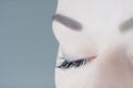 Close-up of closed eye with long artificial eyelashes amazing skin, ideal eyebrow of unrecognizable young woman on grey.