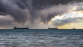 Close-up of a cloudy seascape and a bright sunset. Blue sea, storm clouds with sun rays over the horizon, and several cargo ships Royalty Free Stock Photo