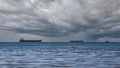 Close-up of a cloudy seascape on a rainy summer day. Blue sea, storm clouds over the horizon, and several cargo ships