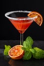 Close-up of cocktail glass with blood orange martini and sugar, with half orange and mint, on black background Royalty Free Stock Photo