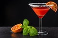 Close-up of cocktail glass with blood orange martini and sugar, with orange and mint stockings, on black background, horizontally, Royalty Free Stock Photo