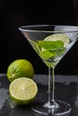 Close-up of cocktail glass with mint leaves and slice of lime on black background with a lime and a half with selective focus Royalty Free Stock Photo