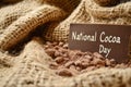 Close-up of cocoa beans and powder on burlap fabric with a chocolate sign for National Cocoa Day.