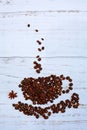 Close- up of coffee beans in the form of a cup, saucer and steam on a light wooden background. Vertical Royalty Free Stock Photo