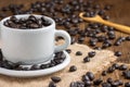 Close-up of coffee cup with white plate with coffee beans, wooden spoon on burlap and wooden table, selective focus Royalty Free Stock Photo