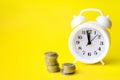 Close-Up Of Coins By Alarm Clock Against Yellow Background. Saving concept, finance concept of time