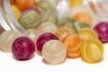 Close-up of colourful sugar balls. The sugar balls roll out of a jar with a lid. White base in the foreground. Blurred balls in