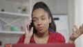 Close-up of confident African American young woman persuading talking on the phone from home office. Intelligent