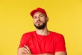 Close-up of confident handsome bearded delivery guy, male courier in red uniform cap and t-shirt, look tough and serious