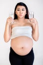 Confused pregnant woman holding milk and water glass