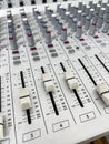 Close up of the control knobs of a gray sound mixer table, with sliders and rotary knobs, background out of focus