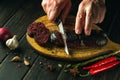 Close-up cook hands with a knife cut blood sausage on a kitchen cutting board. Cooking a national dish with spices at home in Royalty Free Stock Photo