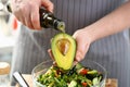 Cook holding bottle with olive oil, watering avocado with bone for cooking healthy salad