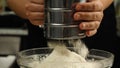 Close-up of a cook sifting flour through a metal sieve into a glass bowl. Side view. The concept of the bakery. Cake Royalty Free Stock Photo