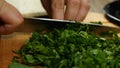 Close-up of a cook slicing parsley with a knife on a cutting board. Side view. Delicious and healthy food.