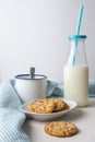 Close-up of cookie and white plate, mug, bottle of milk with straw and blue dishcloth, on white wood