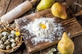 Close up. Cooking Easter cake. Yellow Egg Yolk in a hill of white flour, surrounded by ripe large pears and a bowl of pearl eggs.