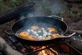 close-up of cooking skillet, with sizzling and popping sounds as eggs are cooked over campfire