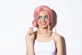 Close-up of coquettish smiling girl in pink wig, looking left intrigued, standing over white background