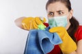 Close-up of a coronavirus model in the hands of a cleaning lady. A housewife in a mask and gloves holds a atomizer and rag.