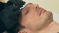 Close up of cosmetologist preparing man for the eyelash extension procedure. High quality close-up of a man laying on a couch
