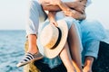 Close up of couple sitting on the stone near the sea or ocean. Photo of hands hugging and holding straw hat. Summer love concept. Royalty Free Stock Photo
