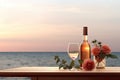 Close up of couple wine champagne glasses and bottle for celebration on wooden table with sea view and sunset sky background,