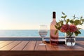 Close up of couple wine champagne glasses and bottle for celebration on wooden table with sea view and sunset sky background,